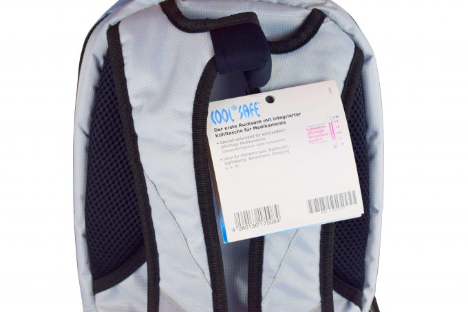 Rückseite des silbergrauen COOL*SAFE-Rucksacks mit schwarzer Rückenpolsterung und Trageschlaufe. Am Träger hängt ein Produktanhänger mit Informationen zur Tasche.