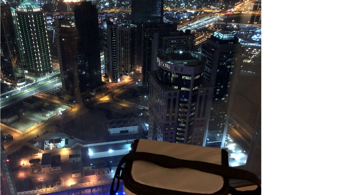 Weiße COOL*SAFE Medikamentenkühltasche vor einem Fenster mit Blick auf die nächtlich erleuchtete Skyline von Qatar.