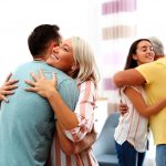 Familie umarmt sich Zwei Generationen umarmen sich herzlich in einem Wohnzimmer – ein älteres Paar begrüßt eine junge Frau und einen jungen Mann.