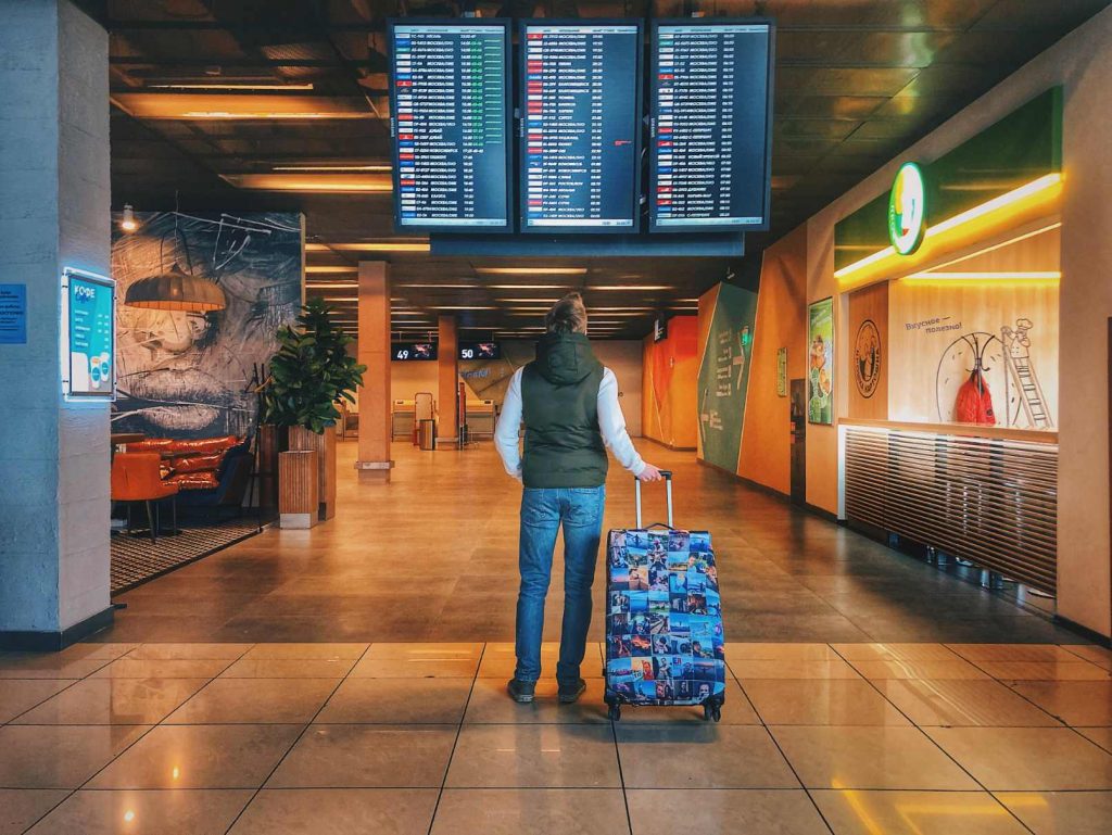 Mann mit Koffer steht vor Anzeigetafel im Flughafen