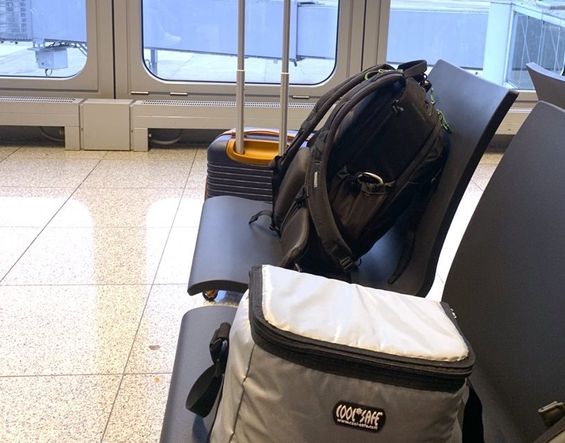 COOL*SAFE Medikamentenkühltasche, Rucksack und Rollkoffer auf Sitzbänken im Wartebereich eines Flughafens.