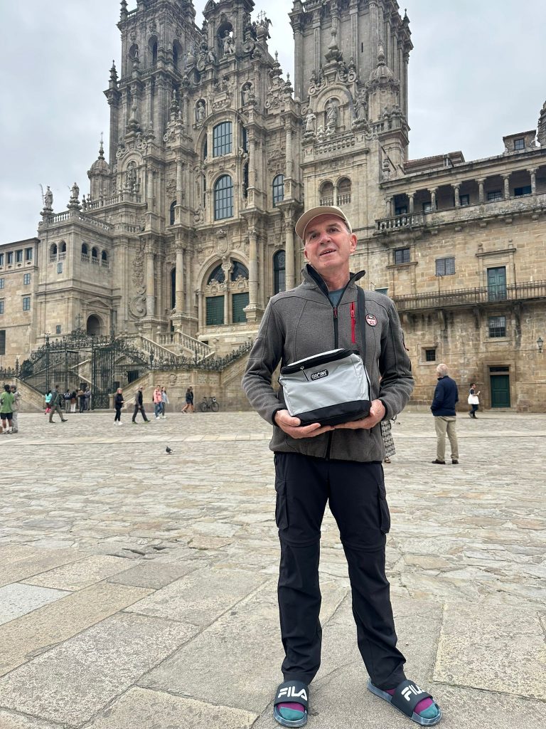 Person steht vor der Kathedrale von Santiago de Compostela und hält eine COOL*SAFE Medikamentenkühltasche in den Händen.
