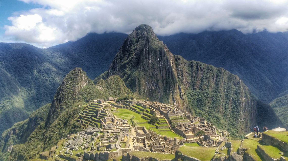 Blick auf die Inka-Ruinenstadt Machu Picchu in Peru, umgeben von grünen Bergketten und Wolken.
