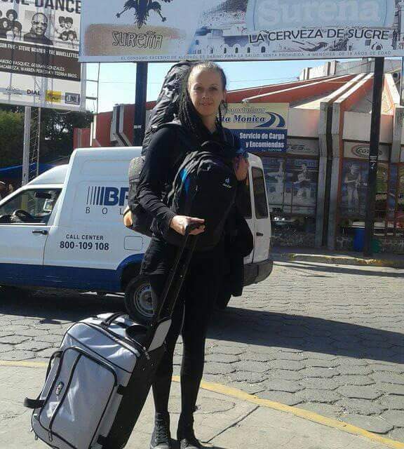 Reisende Frau mit großem Rucksack auf dem Rücken und einer COOL*SAFE Medikamentenkühltasche auf Rollen vor einem Straßenschild in lateinamerikanischer Stadt