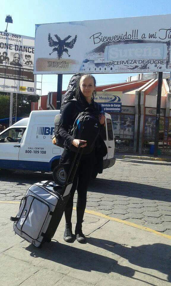 Reisende Frau mit großem Rucksack auf dem Rücken und einer COOL*SAFE Medikamentenkühltasche auf Rollen vor einem Straßenschild in lateinamerikanischer Stadt